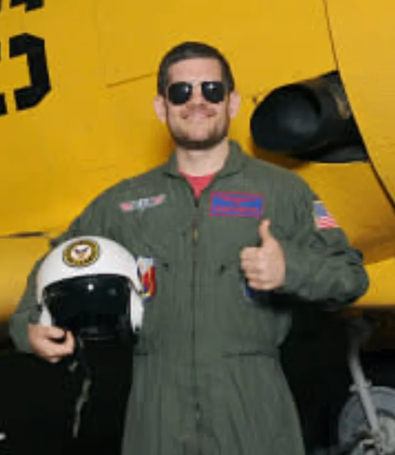 Matthew Brahms in a flight suit beside a yellow training aircraft